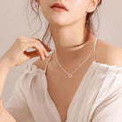 NEWYORKLISTED Valentine’s Day Specials: Woman wearing a delicate necklace with a heart design against a neutral background