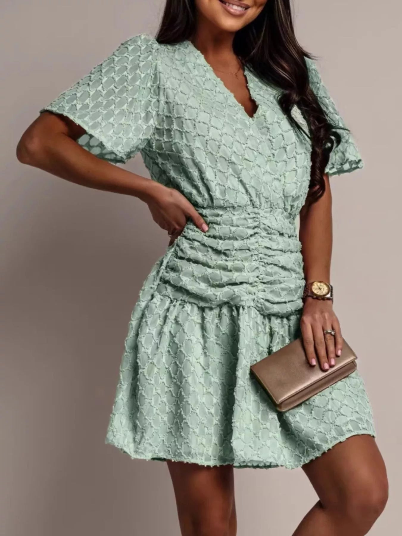 NEWYORKLISTED STYLE COLLECTION: Woman wearing a light green dress with a textured pattern, holding a clutch against a neutral background.