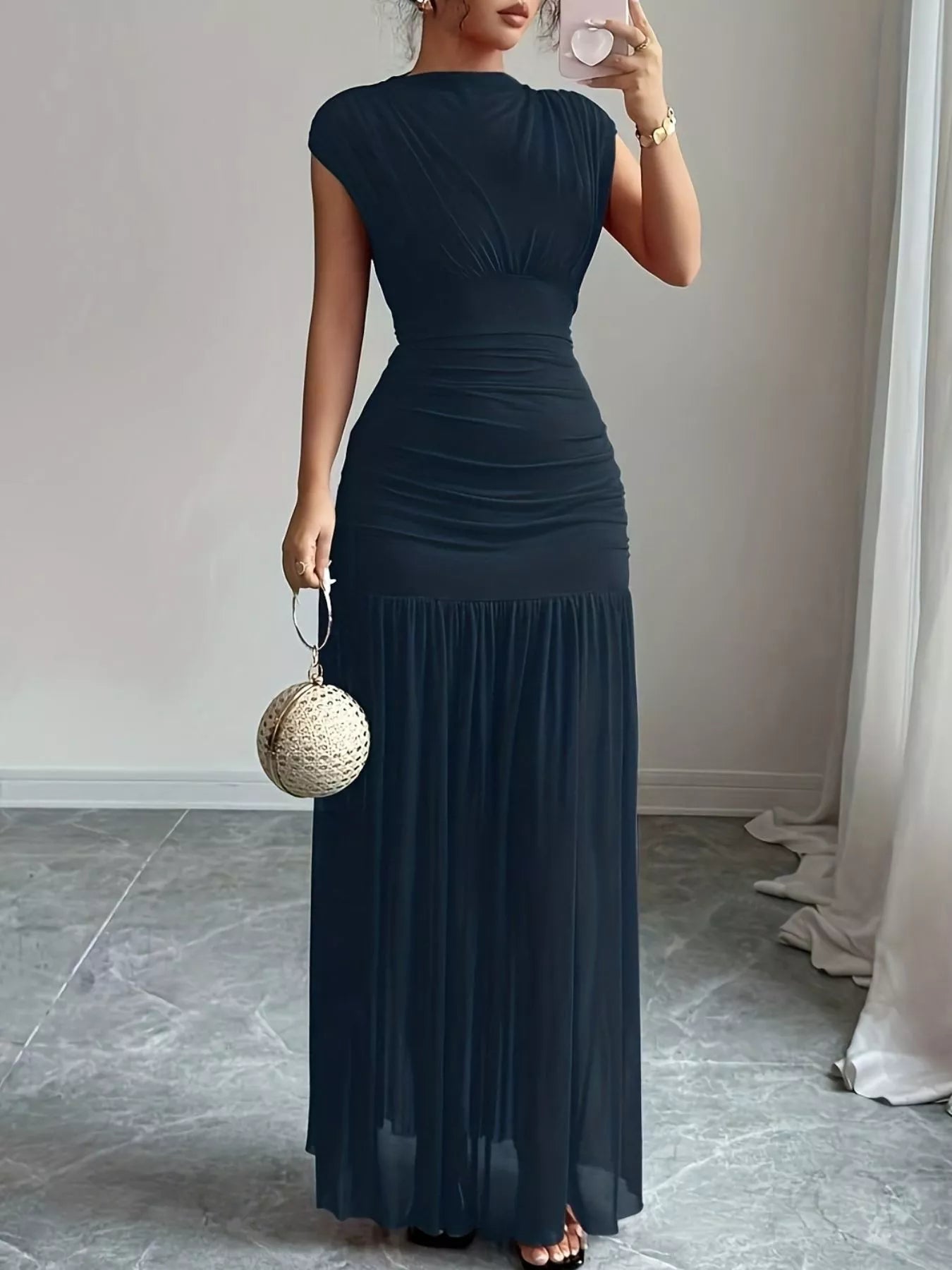 NEWYORKLISTED STYLE COLLECTION: Woman wearing a long dark blue dress holding a small handbag indoors.