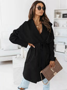 NEWYORKLISTED STYLE COLLECTION: Woman wearing a black coat and sunglasses in a modern living room.