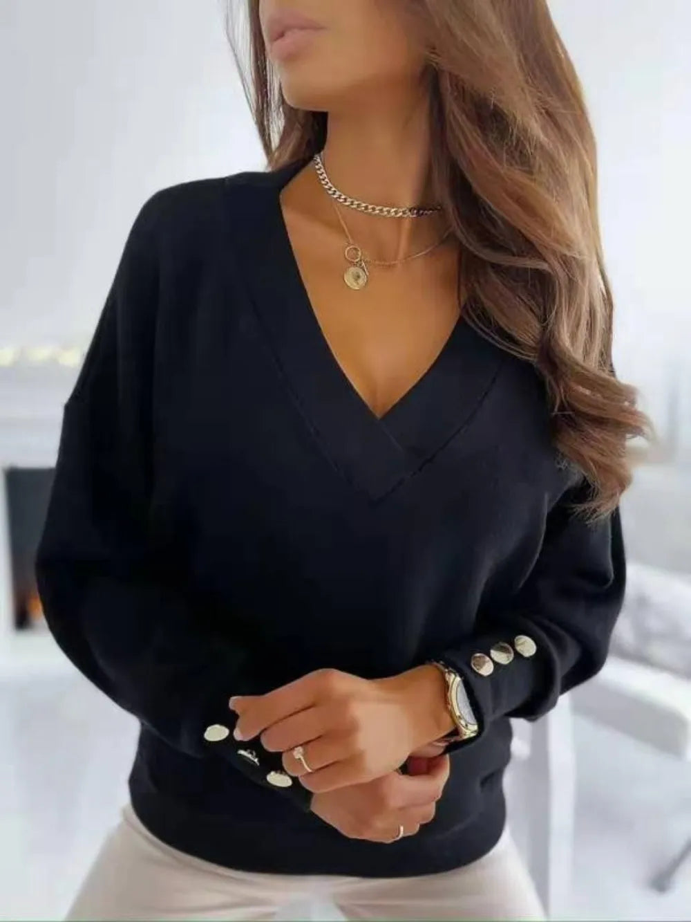 NEWYORKLISTED STYLE COLLECTION: Black sweater with button details worn by a person, on a blurred indoor background