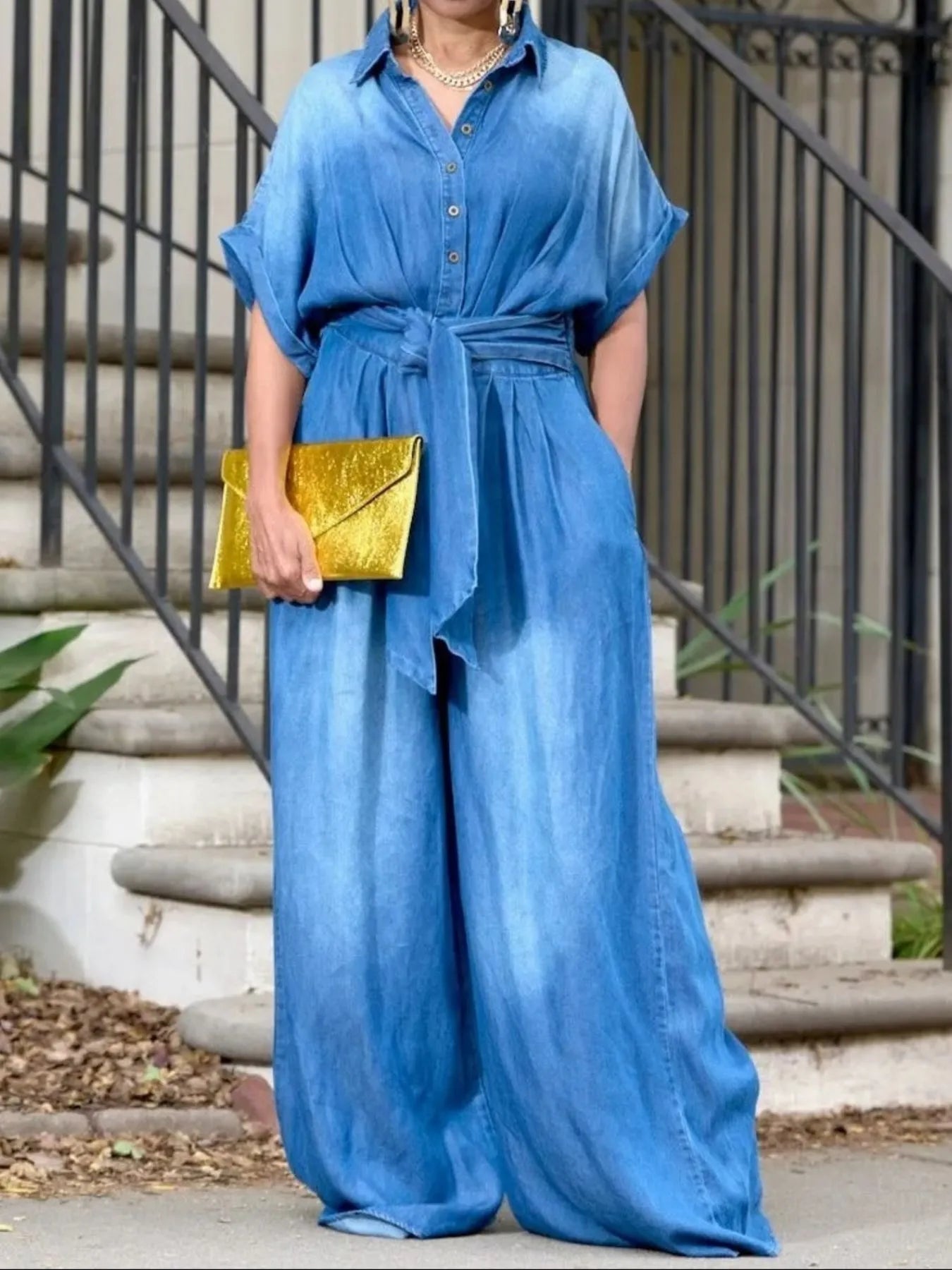 NEWYORKLISTED STYLE COLLECTION: Person wearing a blue outfit with wide-leg pants and a yellow clutch standing on steps.
