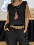 NEWYORKLISTED COMFORT COLLECTION: Person wearing a black sleeveless top with a large pendant necklace and high-waisted black pants.