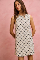 NEWYORKLISTED STYLE COLLECTION: Woman wearing a sleeveless dress with a geometric pattern against a pink background