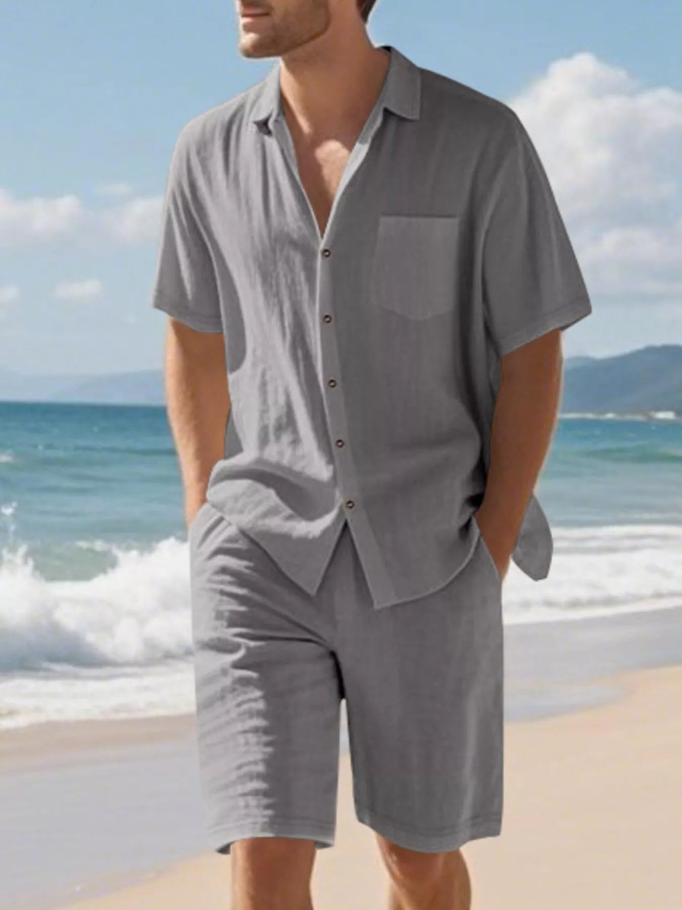 NEWYORKLISTED ATLAS MEN'S COLLECTION: Man wearing a gray shirt and shorts on a beach with ocean and sky in the background