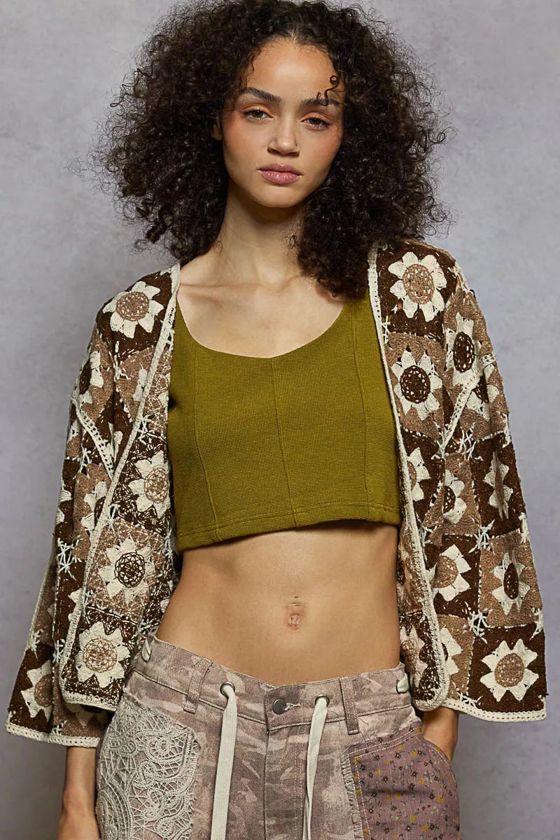 Woman wearing a patterned jacket over a green top and brown pants against a gray background: NEWYORKLISTED STYLE COLLECTION