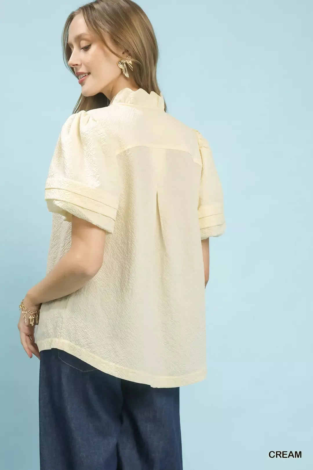 NEWYORKLISTED Style Collection: Woman wearing a cream blouse with short sleeves against a light blue background