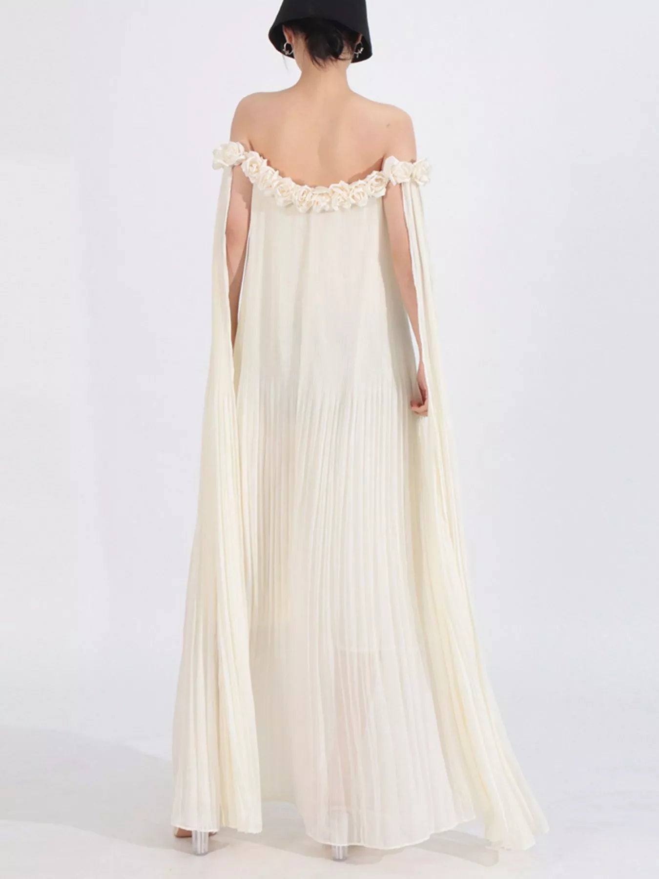 NEWYORKLISTED STYLE COLLECTION: Woman wearing a long, off-shoulder cream dress with floral details on a white background