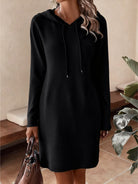 NEWYORKLISTED Comfort Collection: Person wearing a black hoodie dress holding a handbag indoors.
