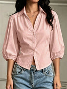 NEWYORKLISTED STYLE COLLECTION: A woman wearing a light pink button-up blouse with voluminous elbow-length puff sleeves and light blue jeans, shown from the neck down against a neutral indoor wall.