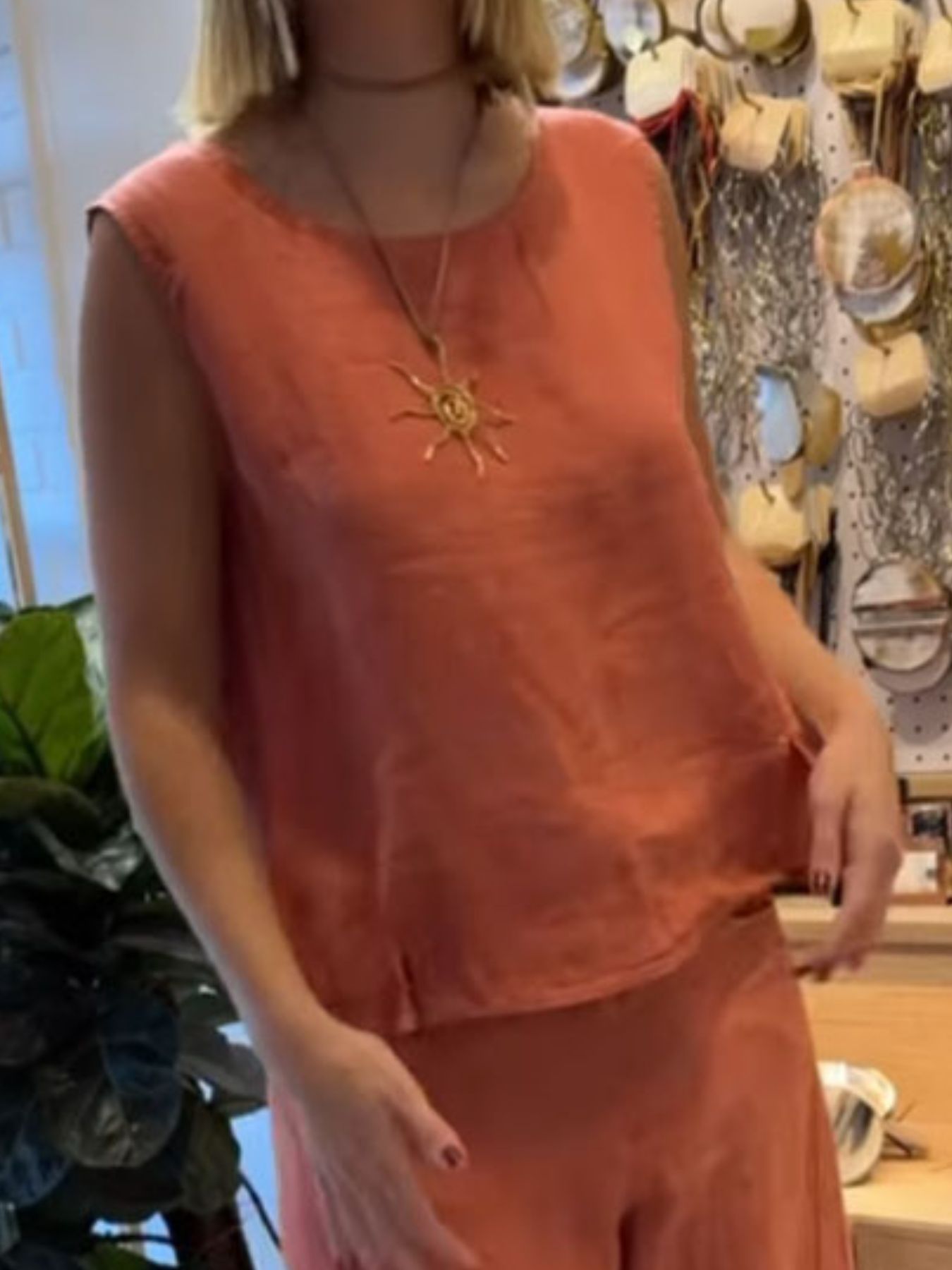 NEWYORKLISTED COMFORT COLLECTION: Person wearing a sleeveless orange top with a sun pendant necklace in a store setting.