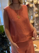 NEWYORKLISTED COMFORT COLLECTION: Person wearing a sleeveless orange top with a sun pendant necklace in a store setting.