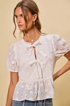 NEWYORKLISTED STYLE COLLECTION:  Woman wearing a white embroidered blouse with puff sleeves against a beige background
