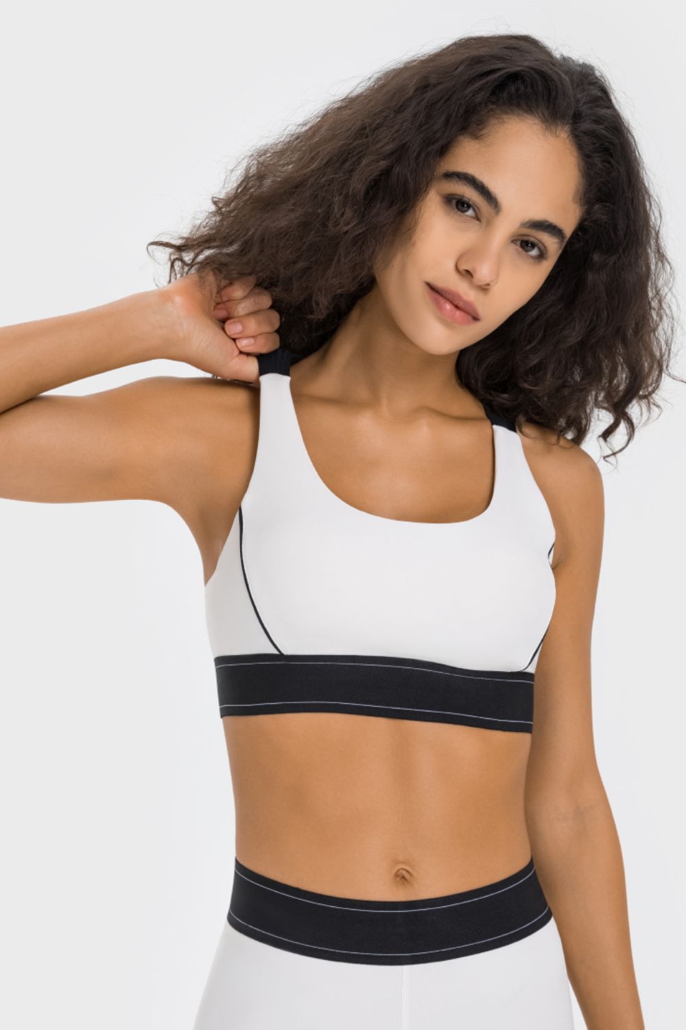 NEWYORKLISTED ACTIVEWEAR COLLECTION: Woman wearing a white sports bra with black accents on a plain background
