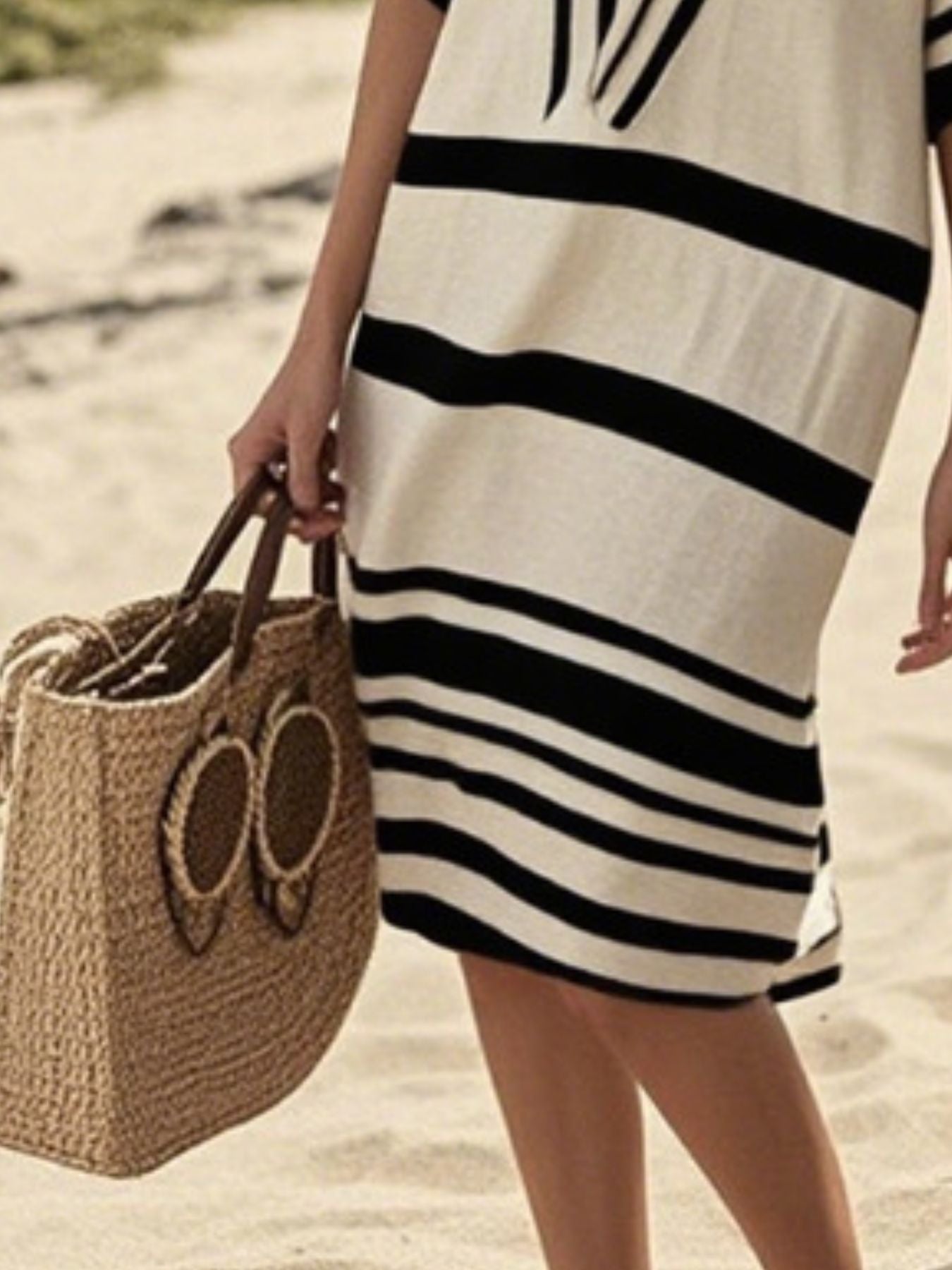 NEWYORKLISTED STYLE COLLECTION: Person wearing a black and white striped dress holding a woven bag on a beach.