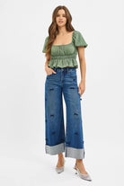 NEWYORKLISTED STYLE COLLECTION: Woman wearing a green top and blue jeans with distressed details on a white background