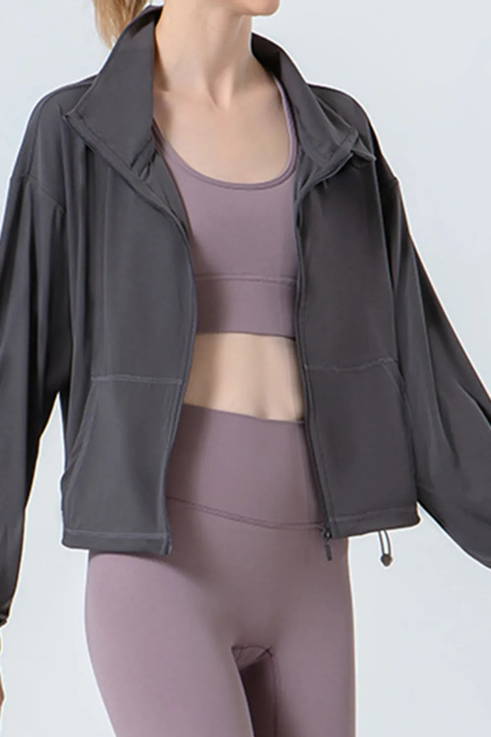 NEWYORKLISTED ACTIVEWEAR COLLECTION: Person wearing a gray jacket over a matching athletic outfit on a plain background