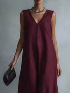 NEWYORKLISTED STYLE COLLECTION: A woman wearing a sleeveless deep burgundy V-neck maxi dress, holding a small black leather clutch against a neutral gray studio background.