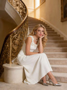 NEWYORKLISTED STYLE COLLECTION: Woman in a white dress sitting on a staircase with ornate railings.