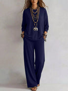 NEWYORKLISTED STYLE COLLECTION: A woman modeling a navy blue two-piece lounge set consisting of a long-sleeve top and matching wide-leg pants, styled with layered gold necklaces and bracelets against a neutral studio background.