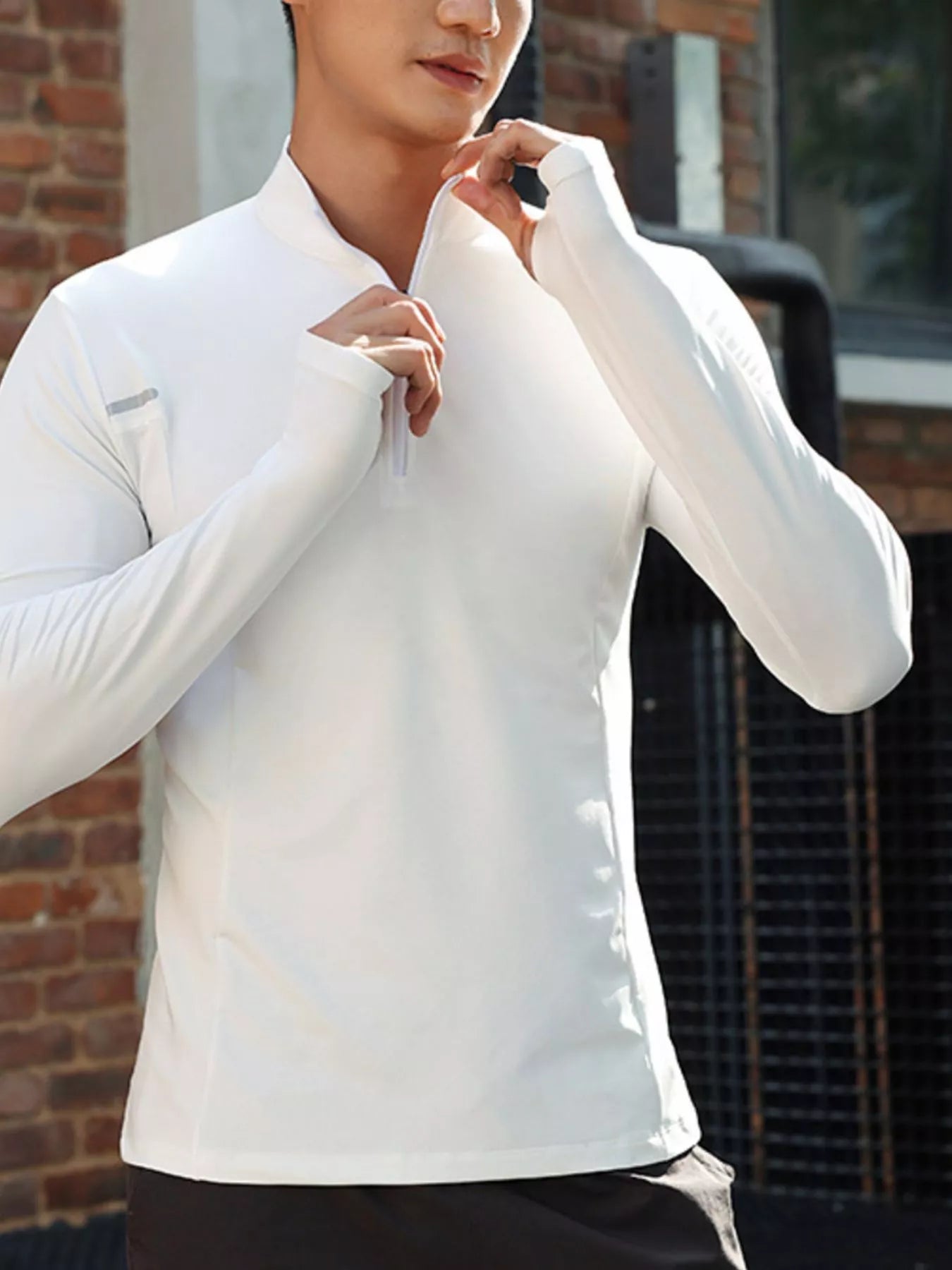 NEWYORKLISTED ATLAS MEN'S COLLECTION: Person wearing a white long-sleeve shirt with a zipper, standing against a brick wall.