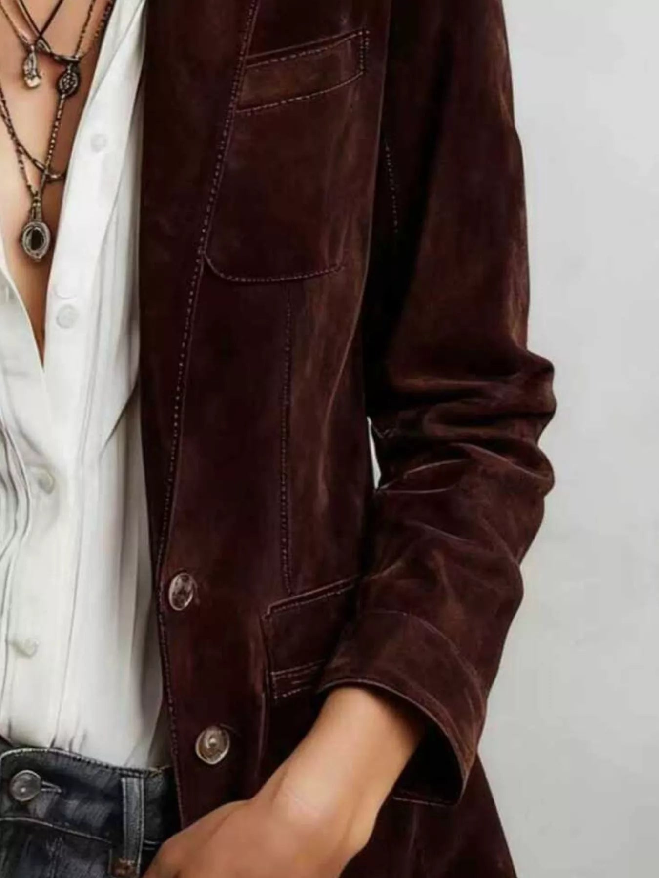 NEWYORKLISTED STYLE COLLECTION: A close-up of a person wearing a dark brown suede or velvet jacket over a white button-up shirt and dark jeans, accessorized with layered necklaces.