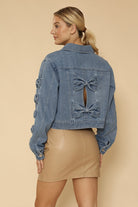 NEWYORKLISTED STYLE COLLECTION: Woman wearing a denim jacket with bow details on a beige background