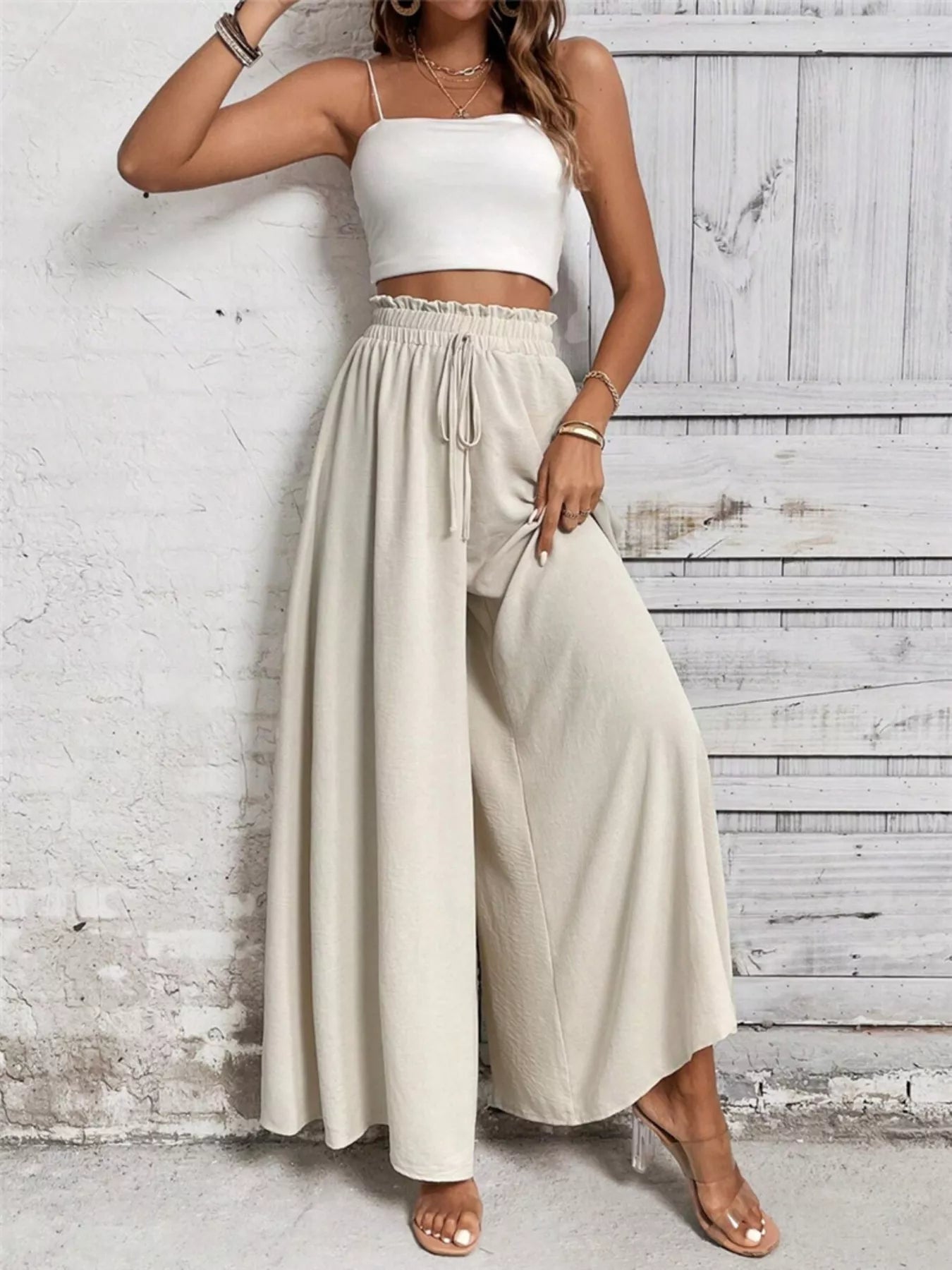 NEWYORKLISTED: Woman wearing a white top and beige wide-leg pants against a light wooden panel background