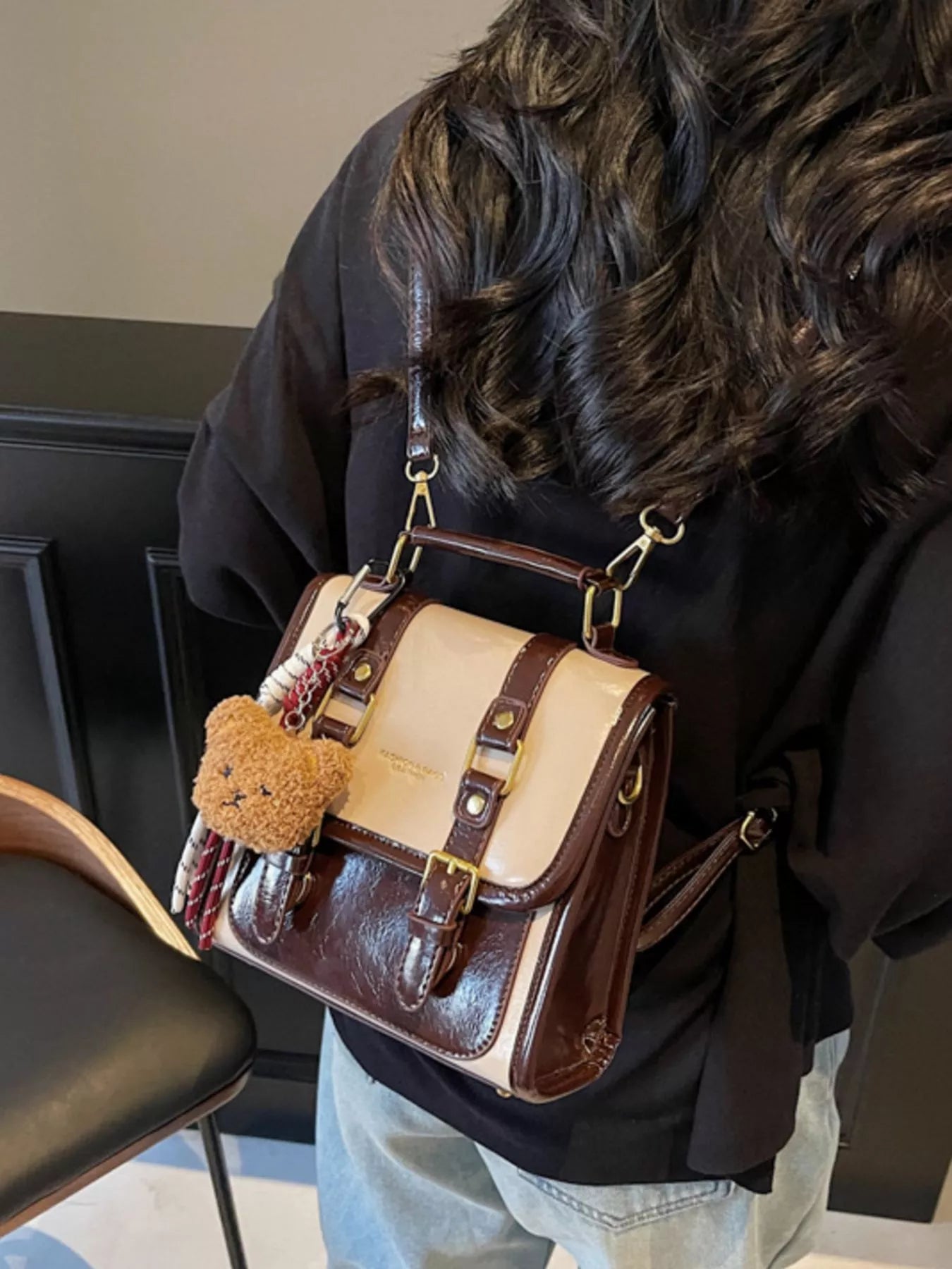NEWYORKLISTED STYLE COLLECTION: Person holding a brown and beige handbag with a teddy bear keychain indoors.