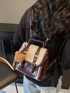 NEWYORKLISTED STYLE COLLECTION: Person holding a brown and beige handbag with a teddy bear keychain indoors.