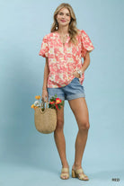 NEWYORKLISTED STYLE COLLECTION: Woman wearing a pink floral blouse and denim shorts, holding a straw bag with flowers against a light blue background.