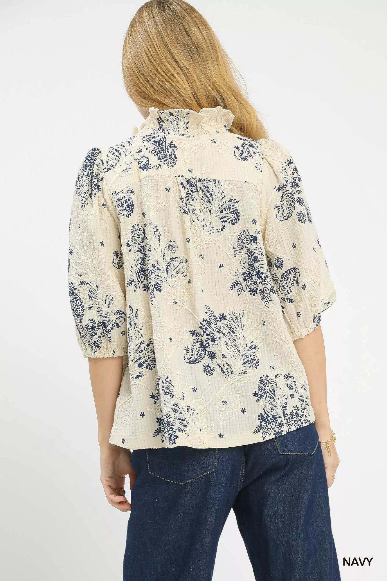 NEWYORKLISTED STYLE COLLECTION: Woman wearing a cream blouse with navy floral pattern and blue jeans on a white background