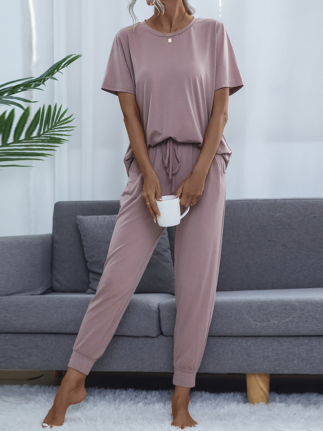 NEWYORKLISTED Intimate Apparel: Person wearing a mauve pajama set sitting on a gray couch with a plant in the background