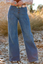 NEWYORKLISTED STYLE COLLECTION: Person wearing blue flared jeans standing on a rocky surface with a blurred natural background