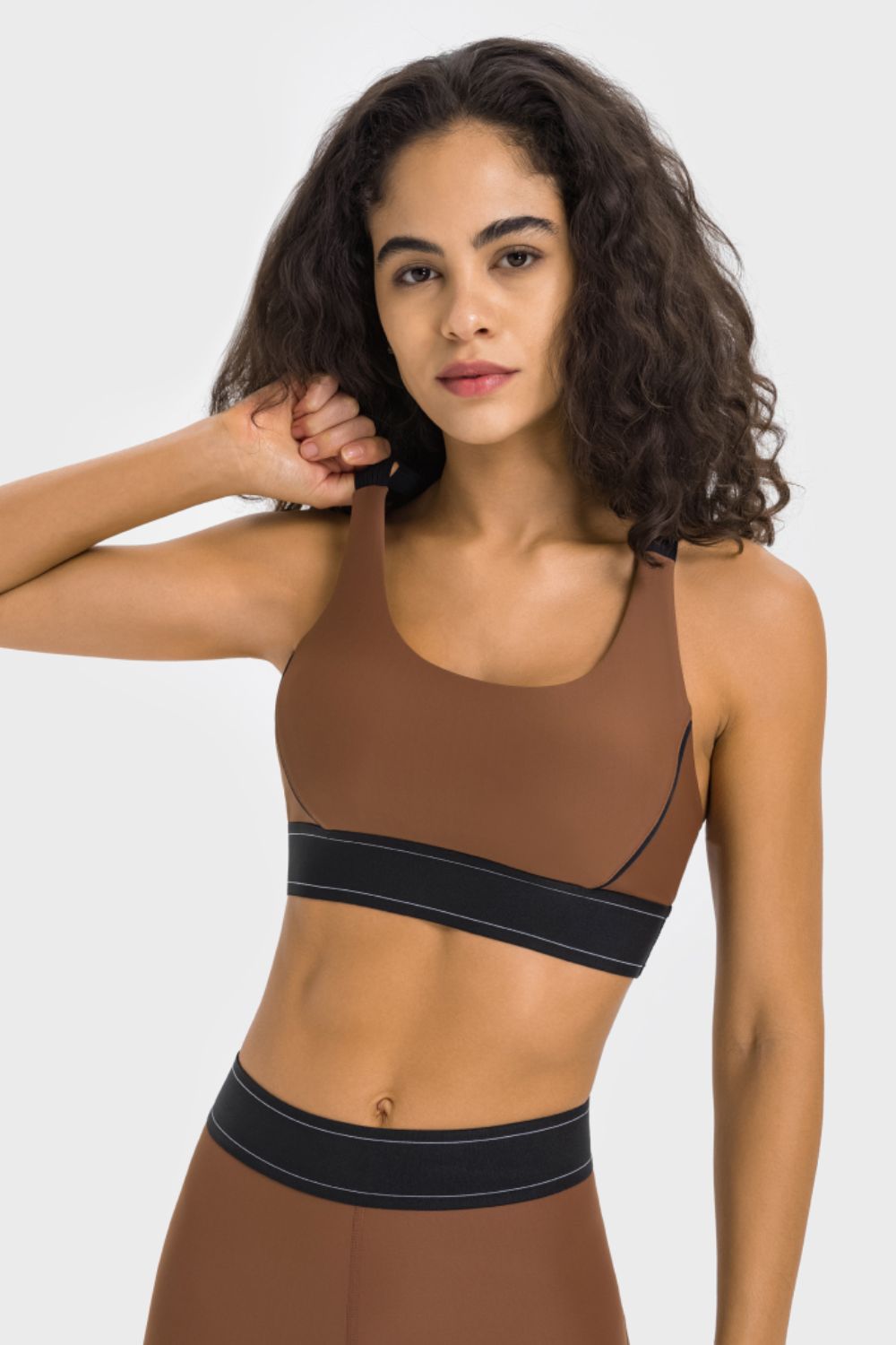 NEWYORKLISTED ACTIVEWEAR COLLECTION: Woman wearing a brown sports bra and leggings with black accents on a white background