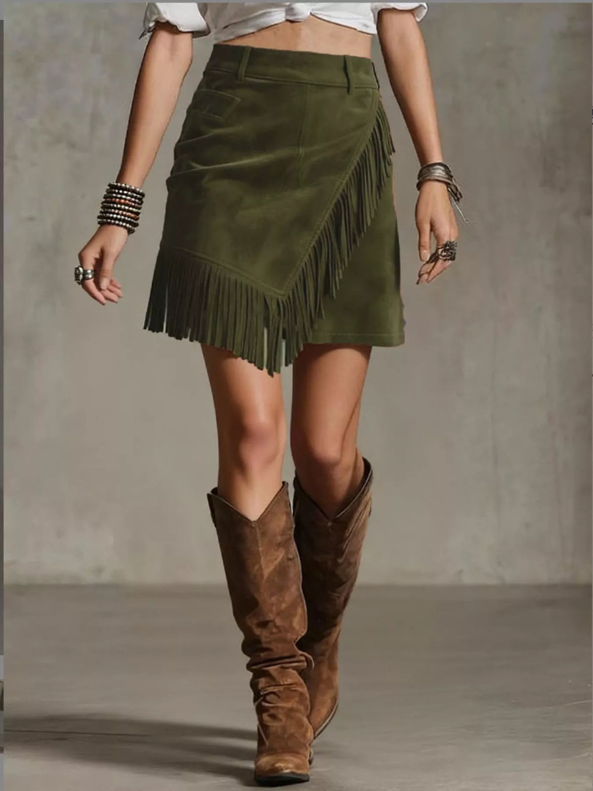NEWYORKLISTED STYLE COLLECTION: Person wearing a green suede skirt with fringe and brown knee-high boots on a plain background