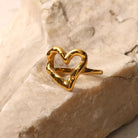 NYLD Glamour Collection by NEWYORKLISTED: Gold heart-shaped ring on a textured beige surface