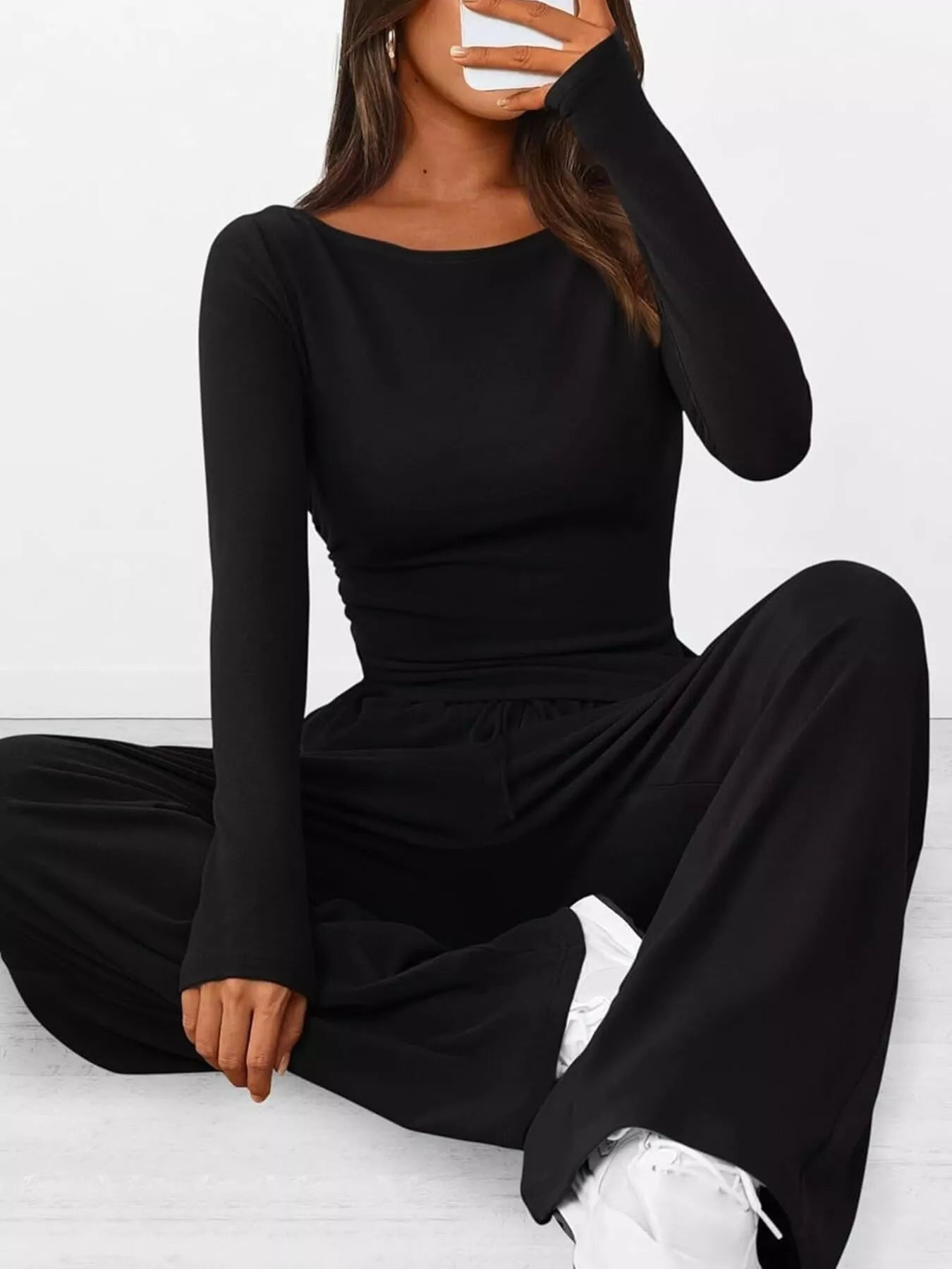 Person wearing a black long-sleeve jumpsuit sitting on a white floor.
