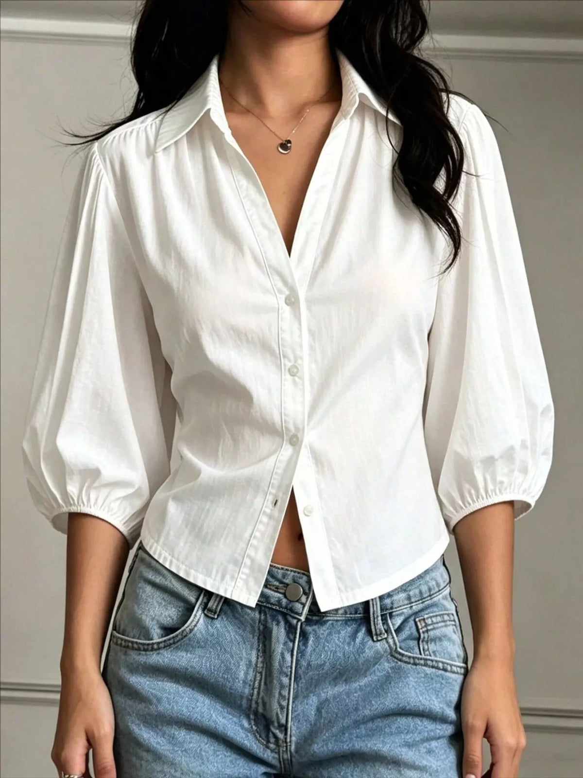 NEWYORKLISTED STYLE COLLECTION: A woman wearing a white long-sleeve button-up shirt with voluminous puff sleeves and light blue jeans, shown from the neck down against a neutral indoor wall.