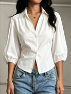 NEWYORKLISTED STYLE COLLECTION: A woman wearing a white long-sleeve button-up shirt with voluminous puff sleeves and light blue jeans, shown from the neck down against a neutral indoor wall.