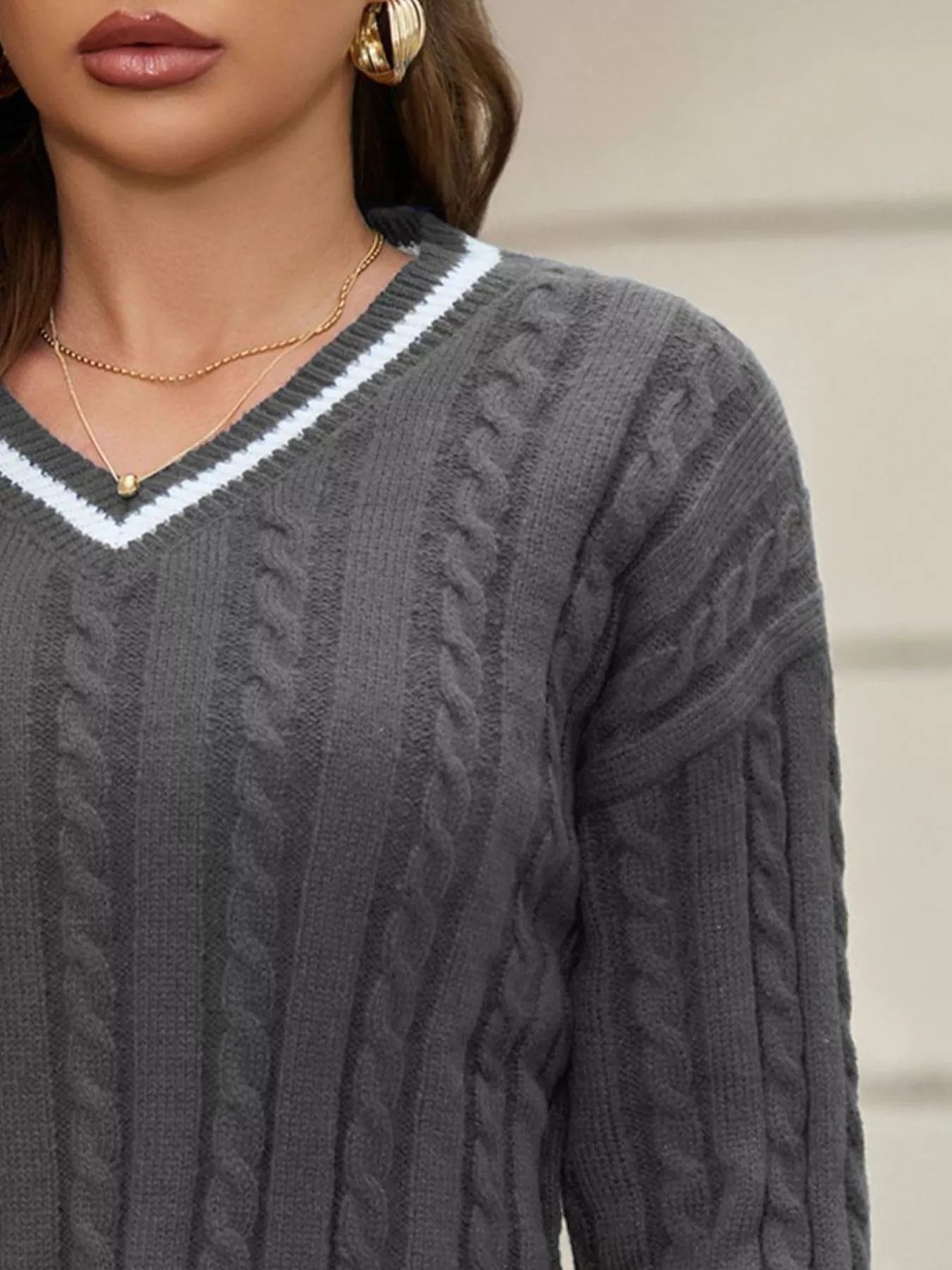 NEWYORKLISTED STYLE COLLECTION: Gray cable knit sweater with a white V-neckline worn by a person.