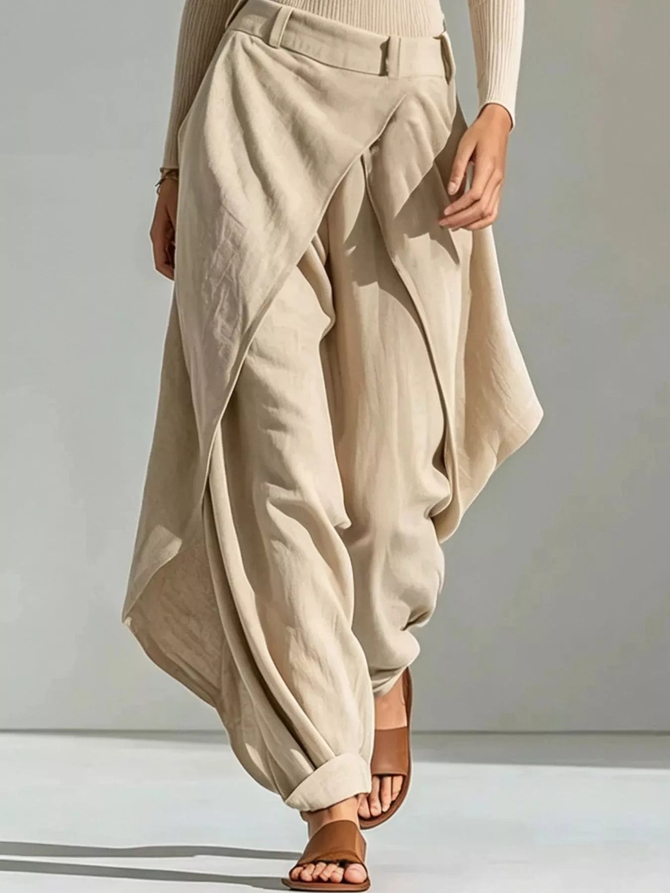 NEWYORKLISTED STYLE COLLECTION: A person wearing loose, draped beige maxi pants with a belted waist, paired with brown slide sandals against a neutral studio background.