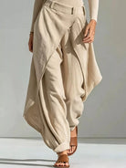 NEWYORKLISTED STYLE COLLECTION: A person wearing loose, draped beige maxi pants with a belted waist, paired with brown slide sandals against a neutral studio background.
