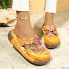 NEWYORKLISTED SHOE COLLECTION: Yellow sandals with floral designs worn by a person on a textured surface.