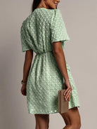 NEWYORKLISTED STYLE COLLECTION: Woman wearing a green patterned dress holding a beige clutch against a neutral background