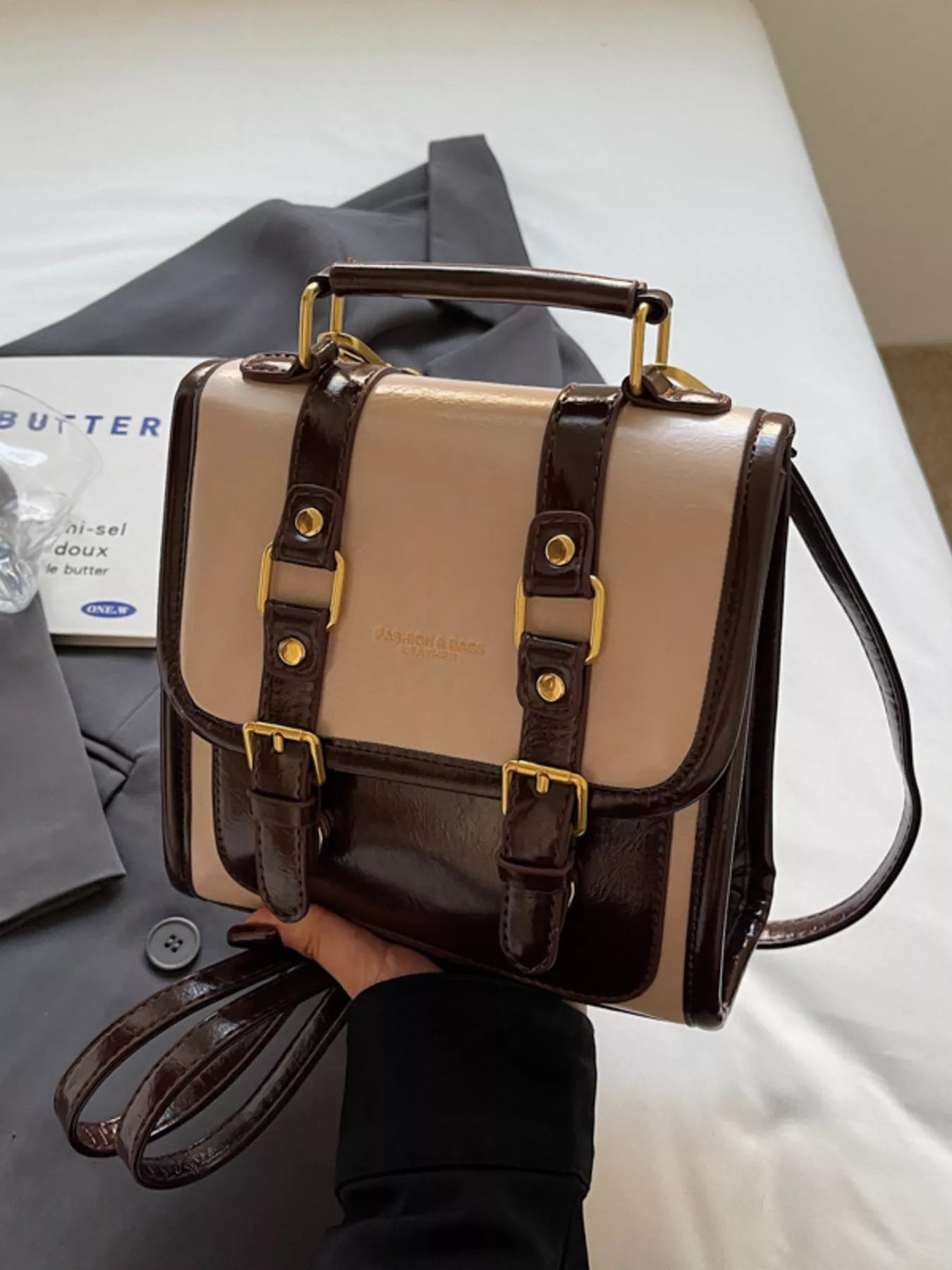 NEWYORKLISTED STYLE COLLECTION: Two-tone handbag with brown and beige colors held by a person, with a magazine in the background.