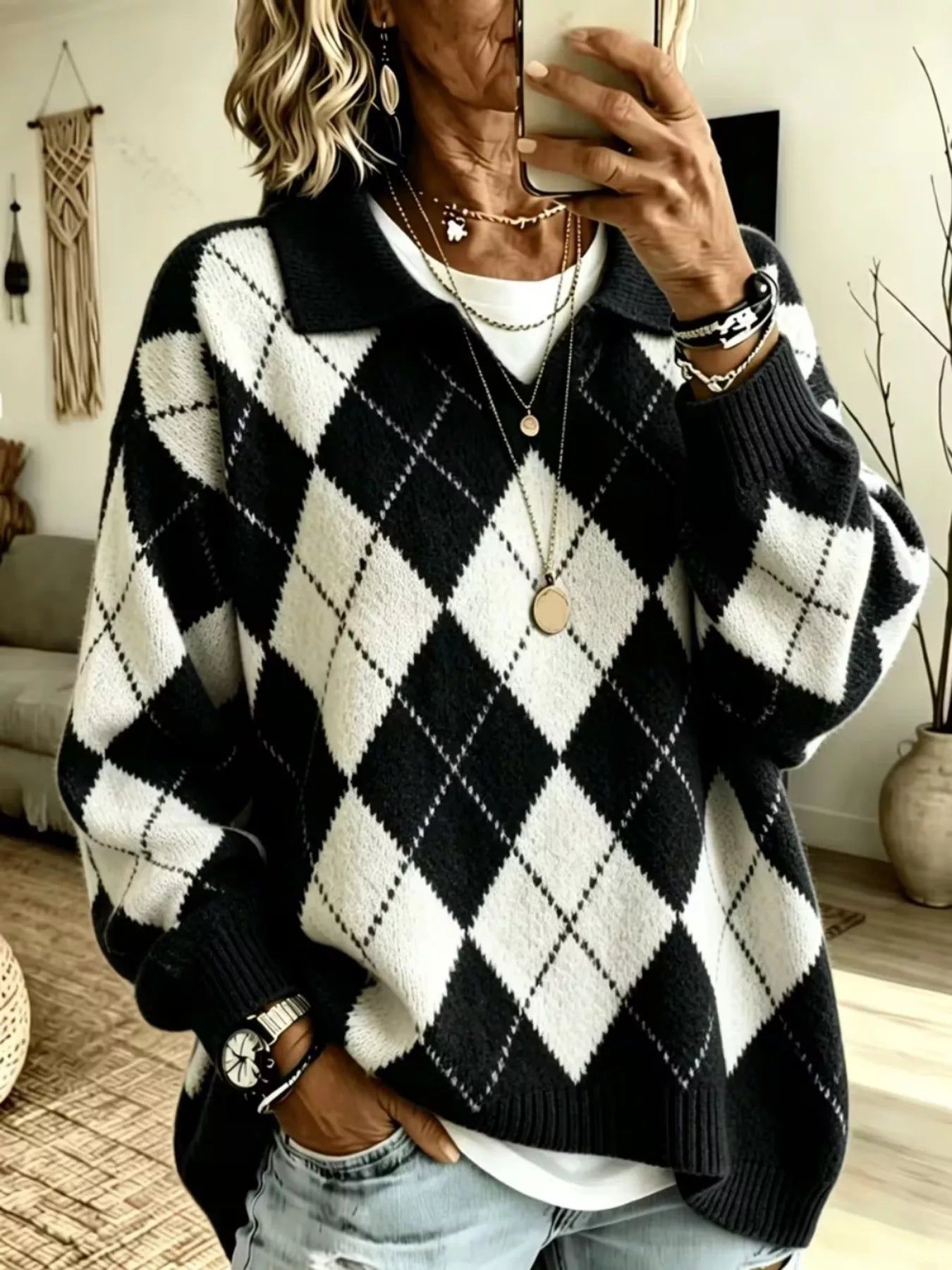NEWYORKLISTED STYLE COLLECTION:A person taking a mirror selfie wearing a black and white argyle knit sweater over a white top, paired with light blue jeans and layered gold necklaces.