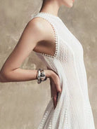 NEWYORKLISTED STYLE COLLECTION: Woman wearing a white dress with a textured back design, holding her arm with a bracelet.