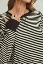 NEWYORKLISTED COMFORT COLLECTION: Close-up of a woman wearing a black and ivory striped knit sweater with dark brown ribbed trim and a matching fingerless glove, against a light gray background.