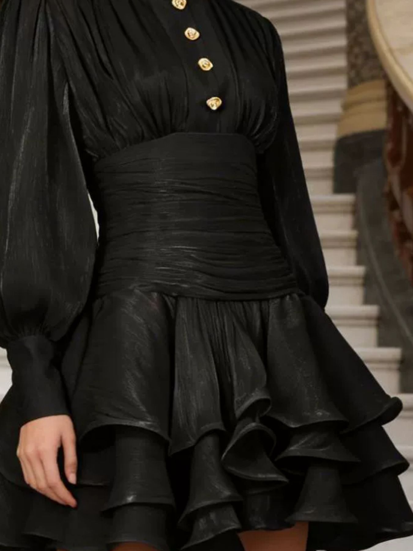 NEWYORKLISTED STYLE COLLECTION: Black dress with gold buttons worn by a person, standing on a staircase.